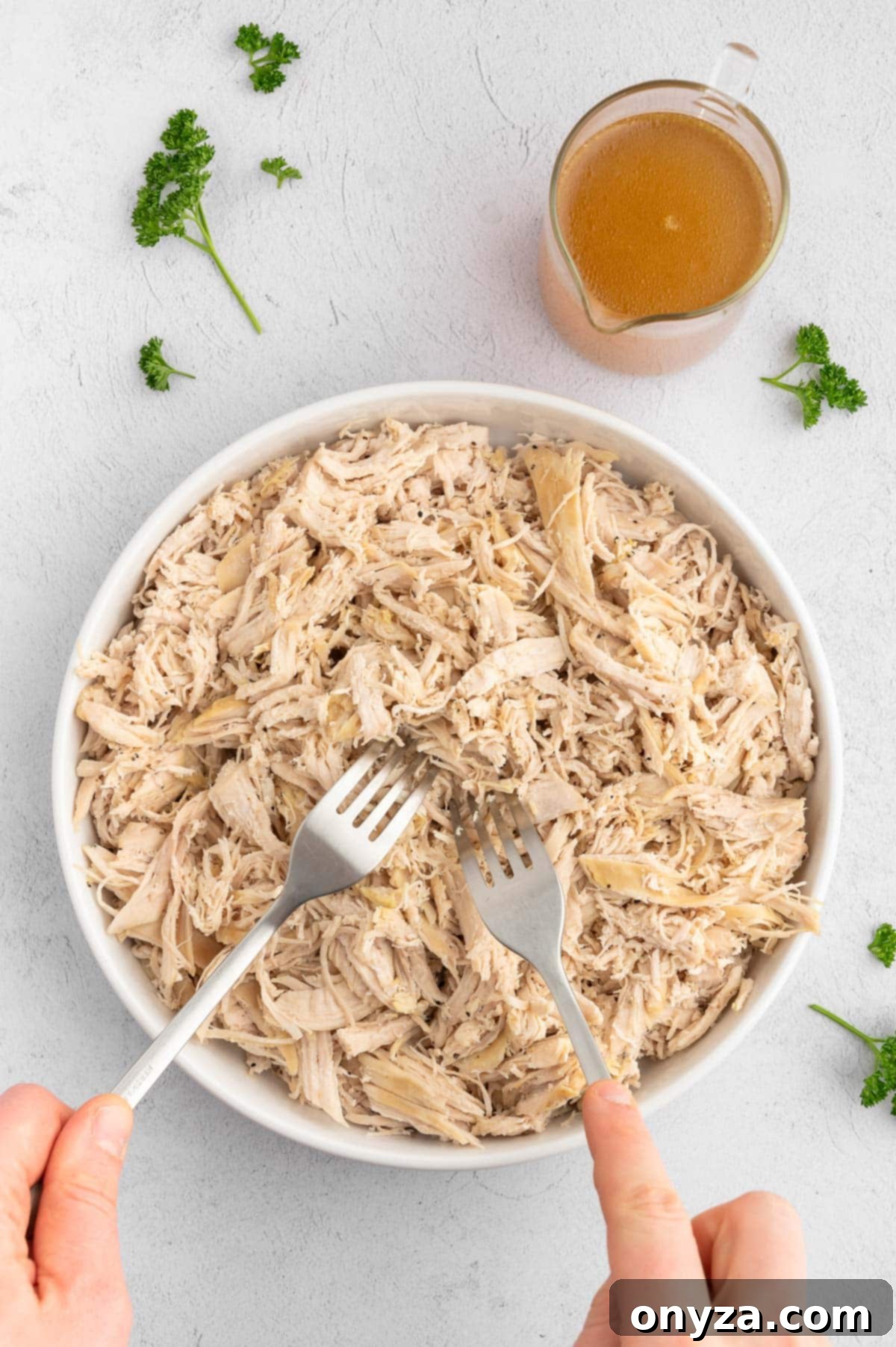 shredding chicken breasts in a white ceramic bowl with two stainless steel forks