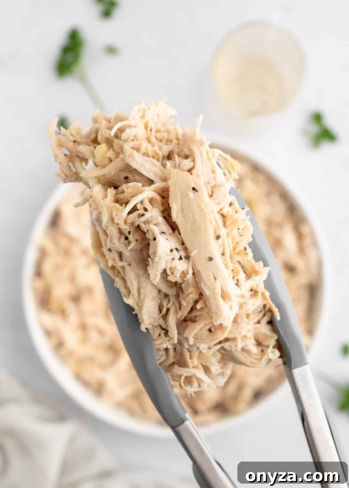 closeup of a scoop of shredded chicken in gray silicone tongs