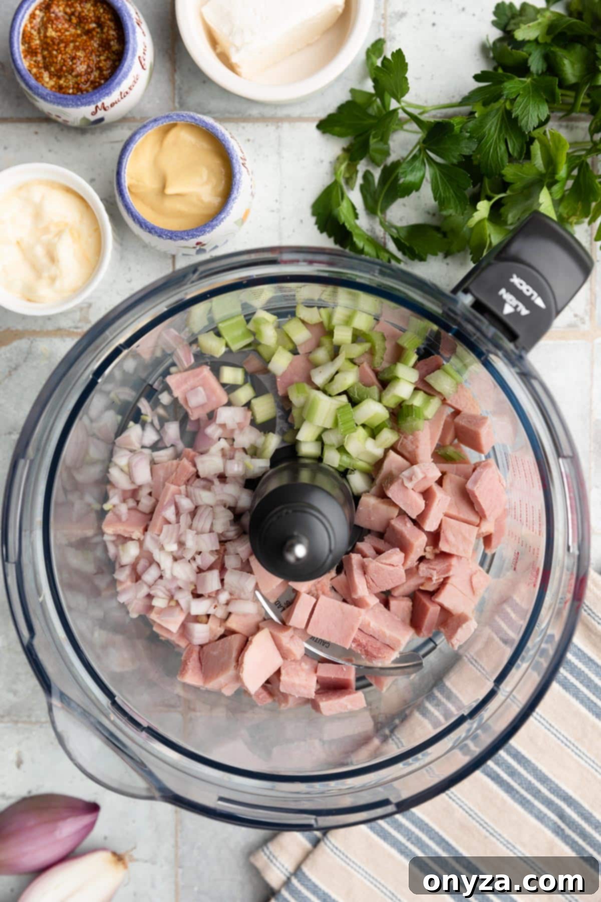 Overhead photo of roughly chopped ham, celery, and shallots placed in the bowl of a food processor, ready for the initial pulse.