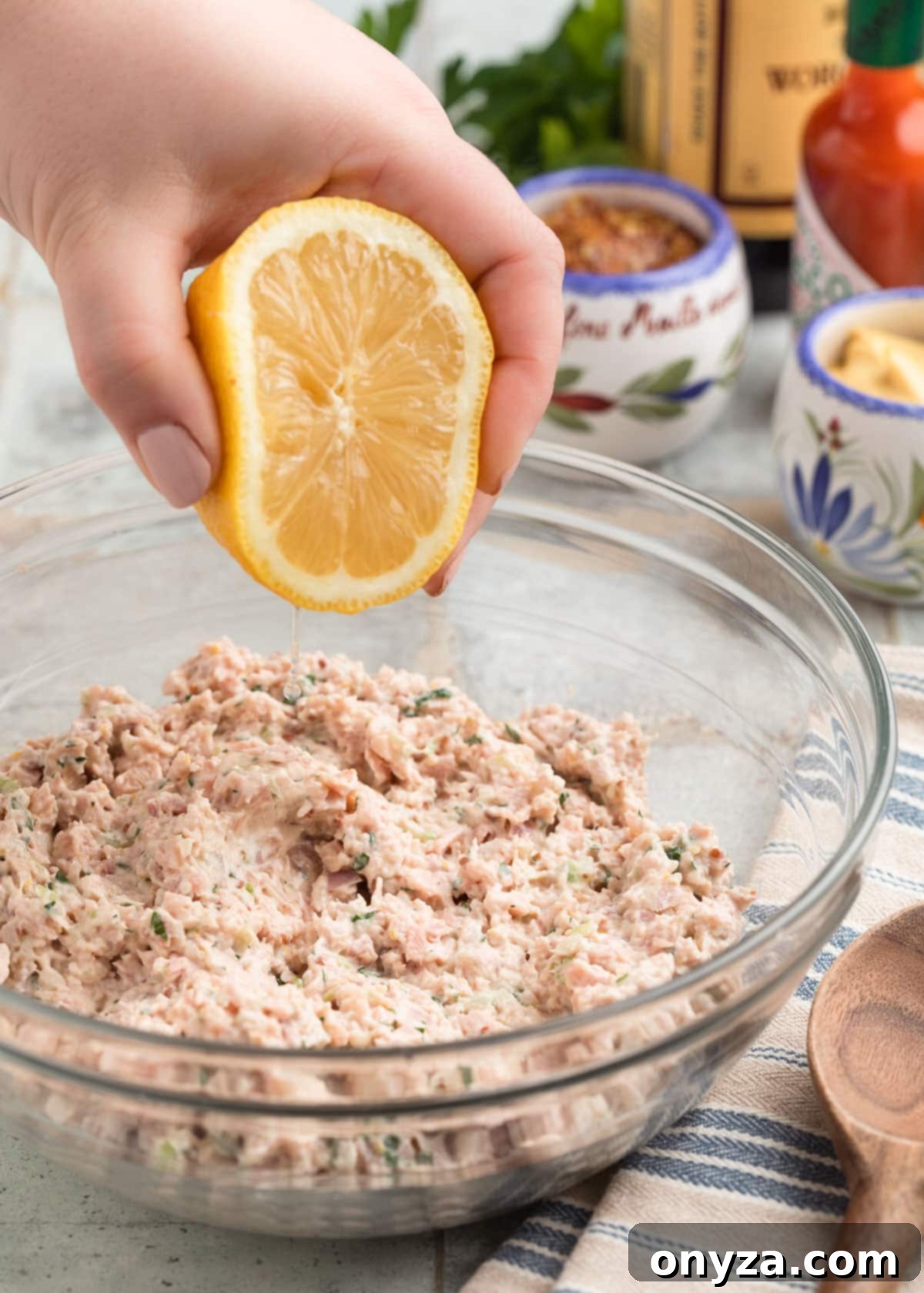 Close-up of fresh lemon juice being squeezed into a glass bowl of Deviled Ham spread, adding a bright, tangy finish.