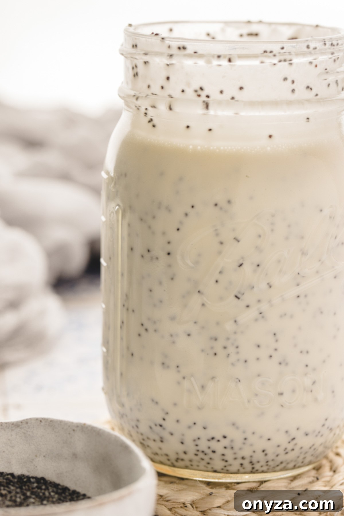 Velvet Poppy Seed Dressing 6 A mason jar of creamy poppy seed dressing sits next to a small bowl of poppy seeds on a blue and white tiled surface.