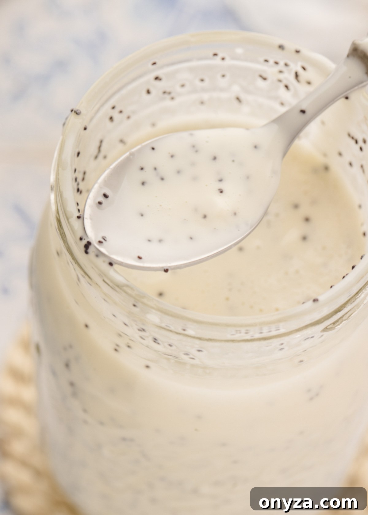 Velvet Poppy Seed Dressing 7 A mason jar of creamy poppy seed dressing, with a spoonful of the dressing held at the mouth of the jar, showing its creamy texture and poppy seeds.