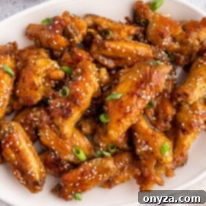closeup of baked honey garlic chicken wings on a white platter, garnished with sesame seeds and scallions