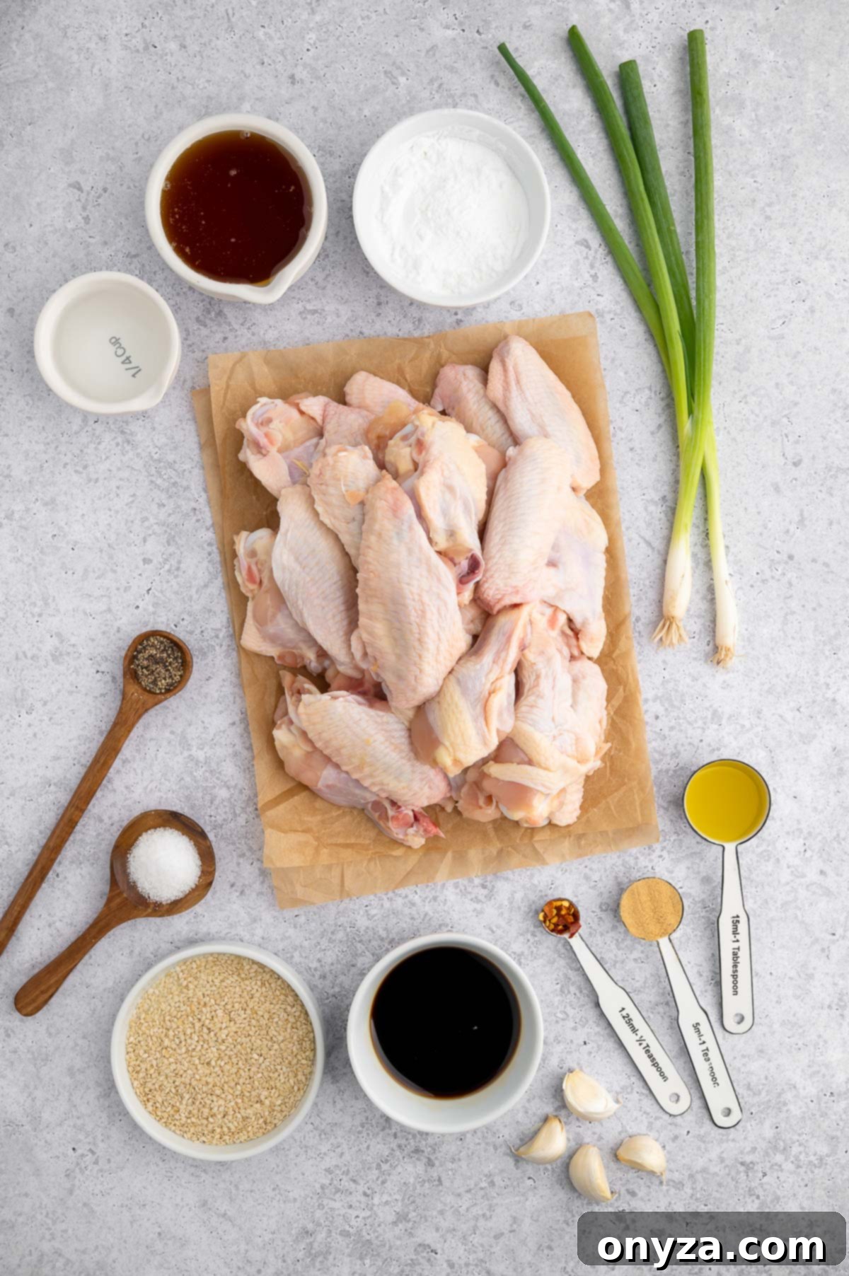 raw chicken wings on a piece of parchment paper surrounded by ingredients to make honey-garlic wing sauce in bowls