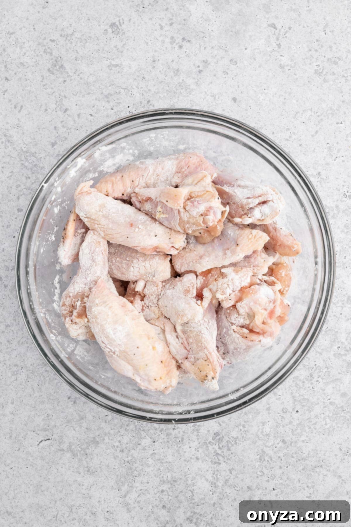 raw chicken wings in a glass bowl coated with cornstarch and seasonings