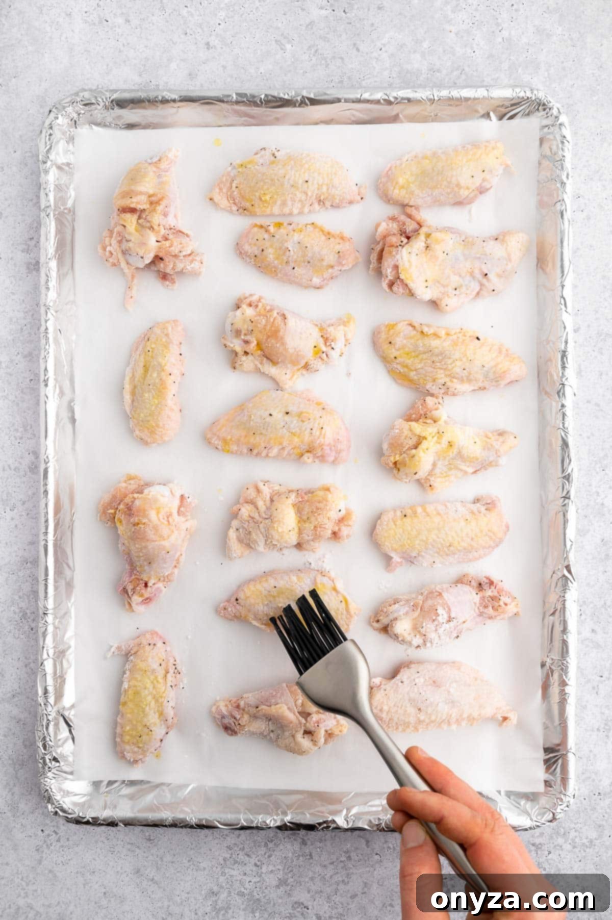 brushing raw chicken wings on a lined sheet pan with oil