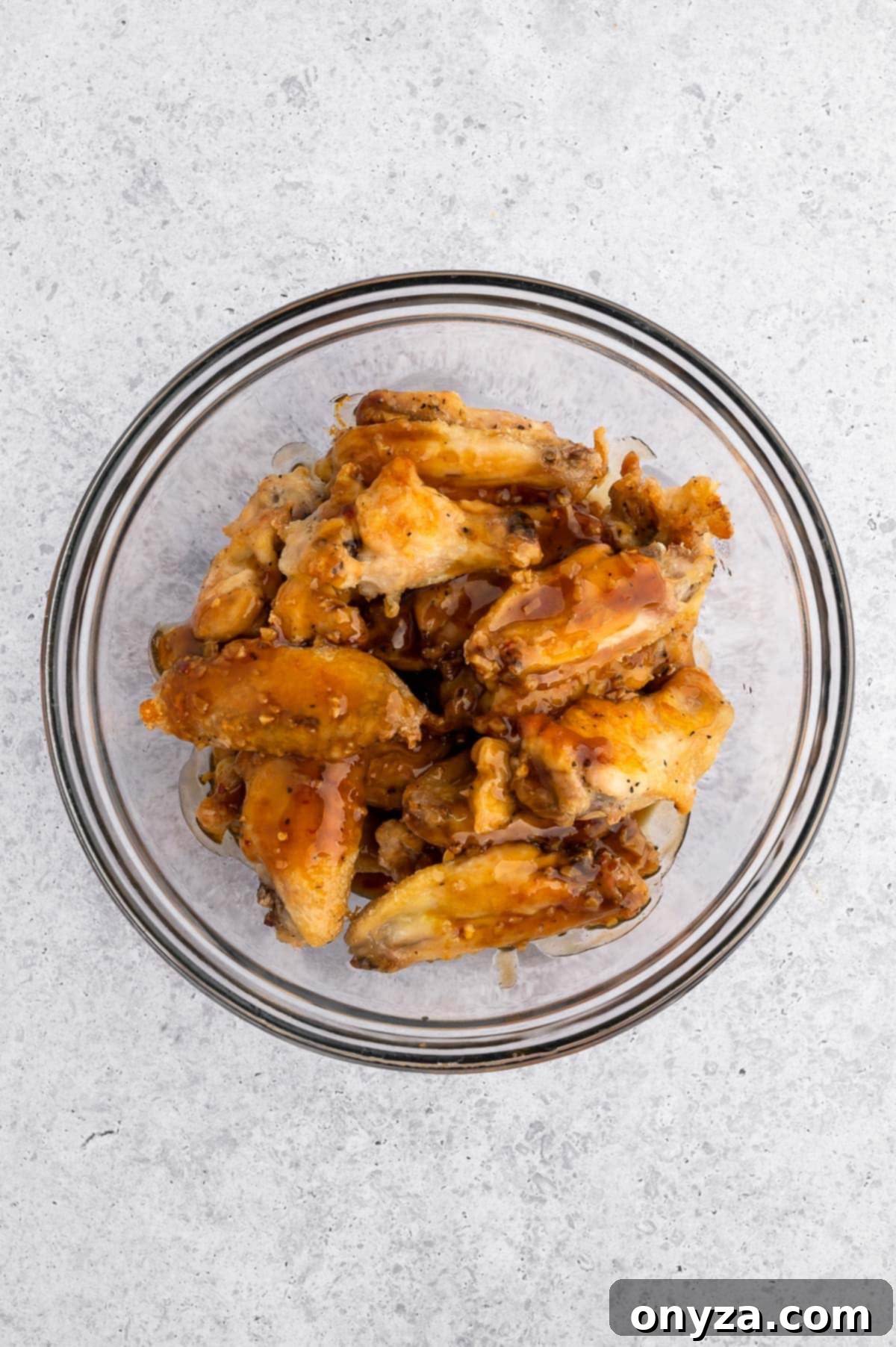 baked chicken wings in a glass bowl with honey garlic sauce poured over the top