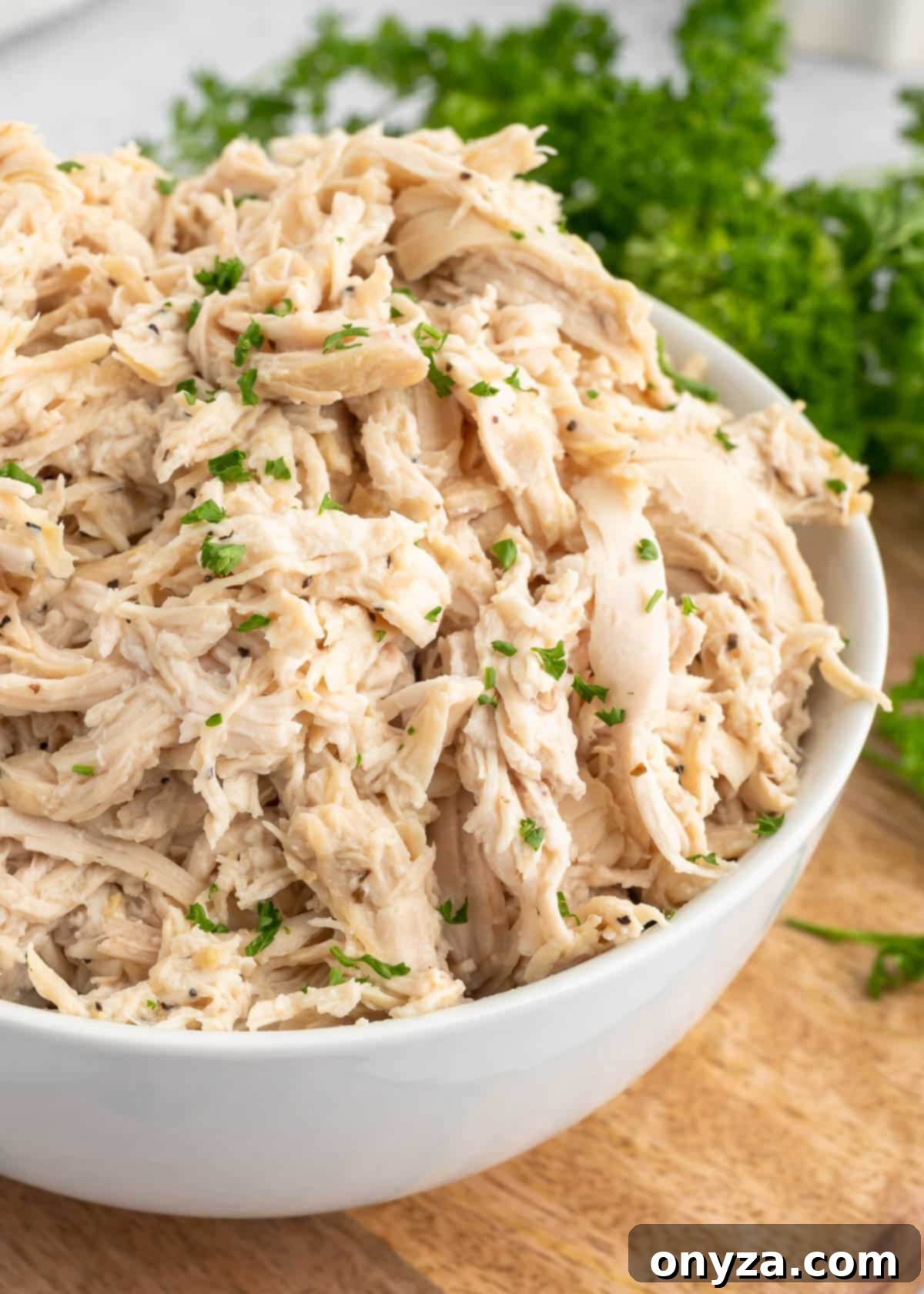 Instant Pot Shredded Chicken in a white bowl, garnished with fresh parsley, resting on a rustic wood cutting board next to a small white bowl of spices
