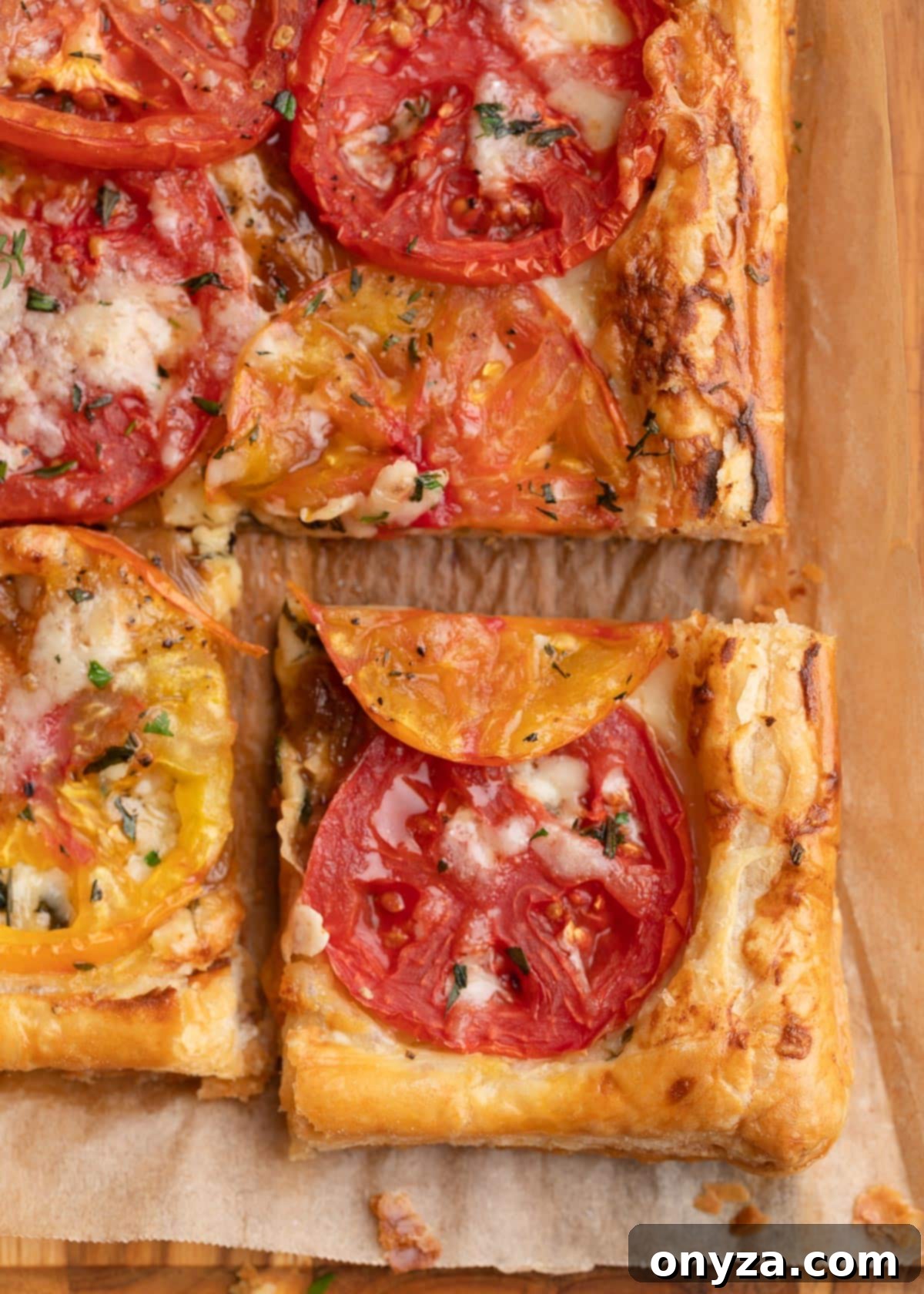 Flaky Tomato Tart 11 overhead closeup of a sliced puff pastry tomato tart on a parchment-lined wooden board