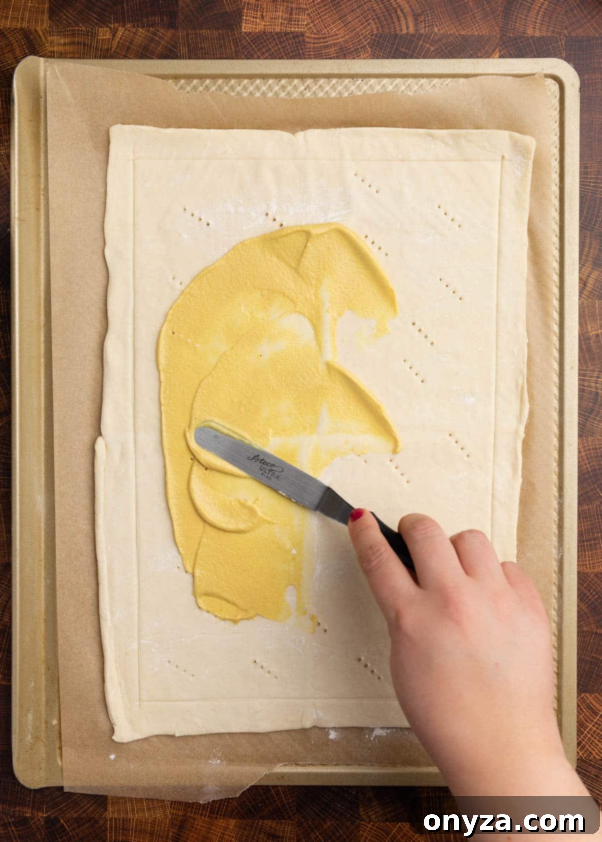 Flaky Tomato Tart 7 overhead photo of spreading Dijon mustard onto a puff pastry dough on a parchment lined baking sheet