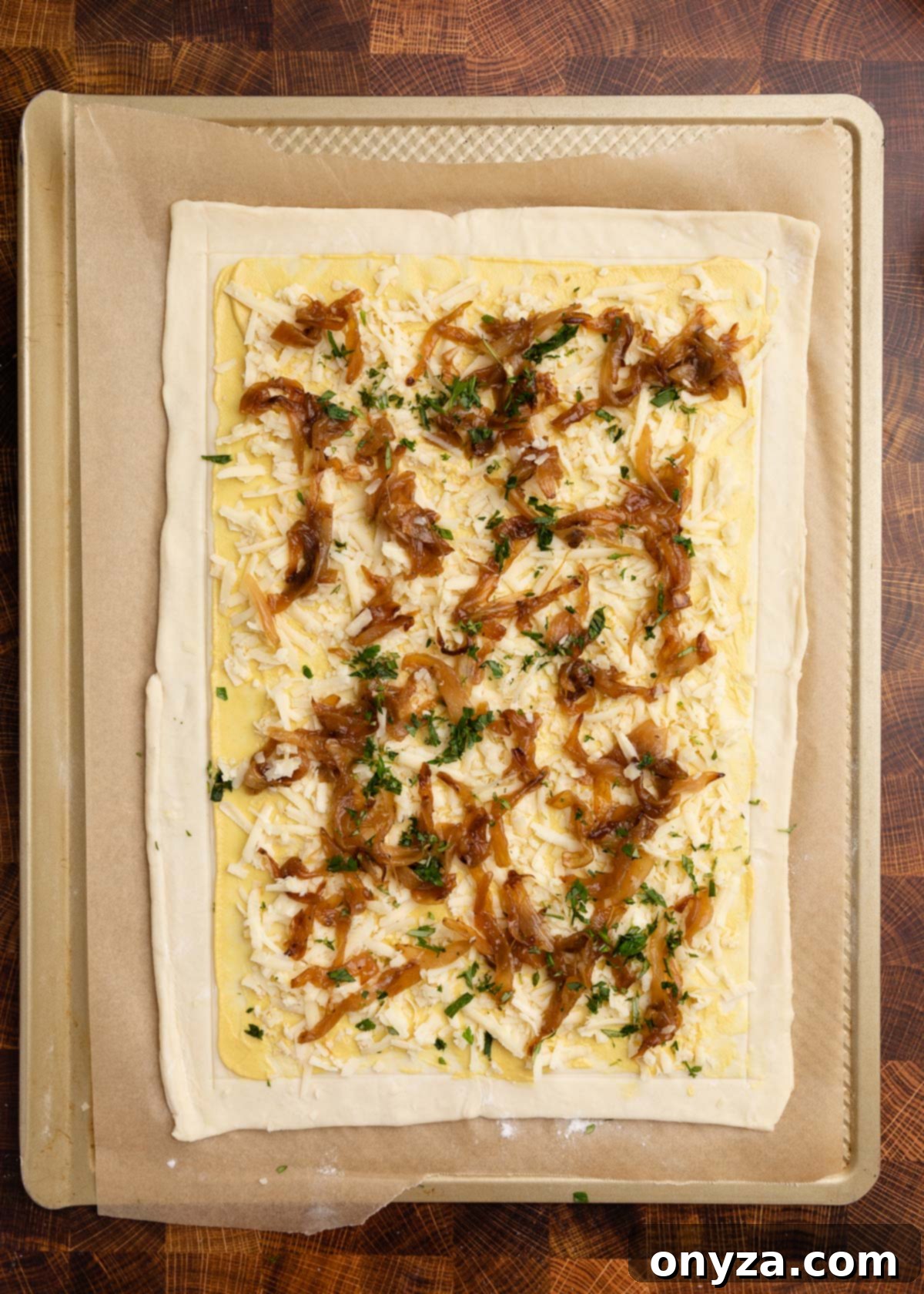 Flaky Tomato Tart 8 overhead photo of puff pastry on a parchment lined baking sheet, topped with Dijon, shredded gruyere, caramelized onions, and herbs