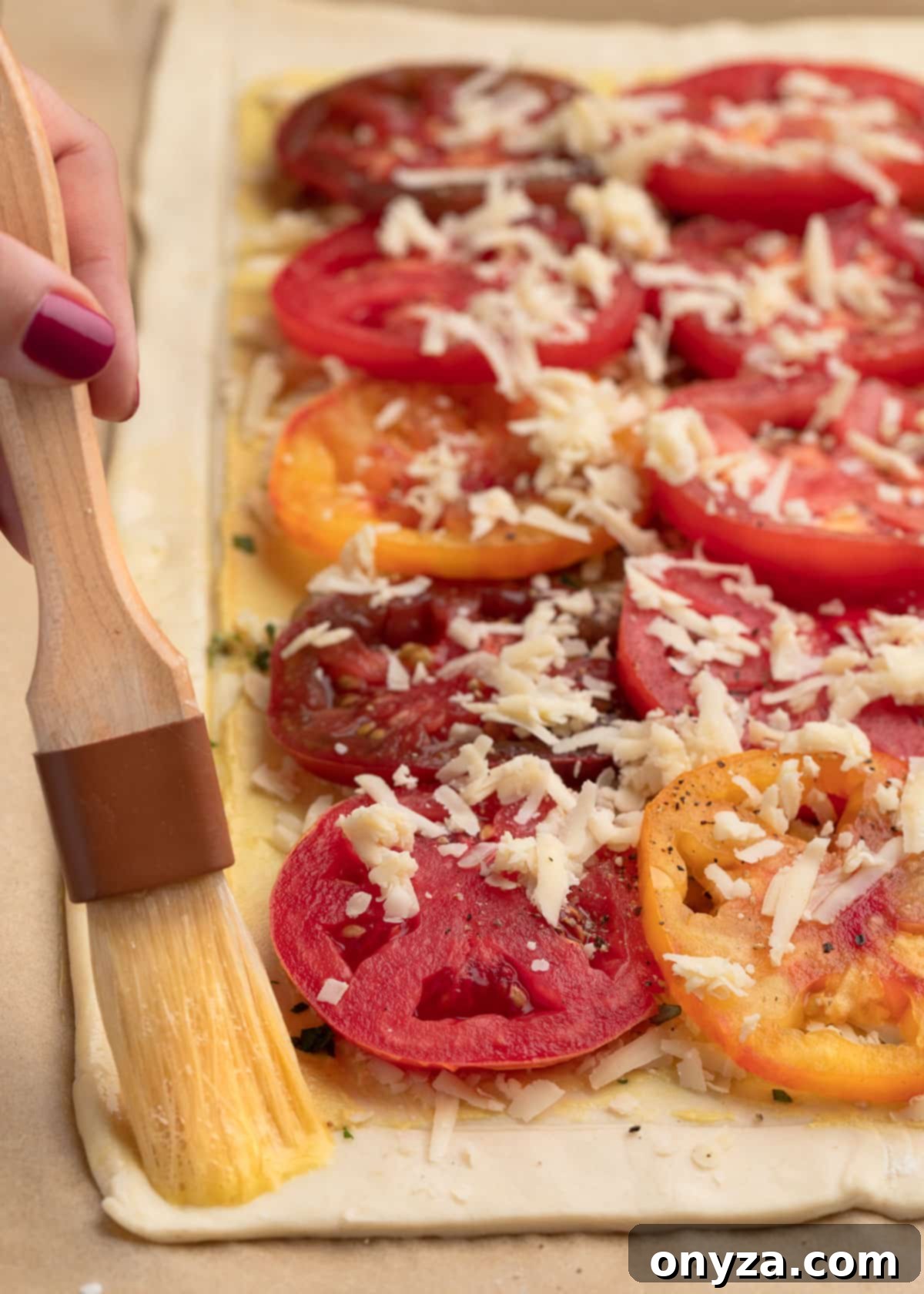 Flaky Tomato Tart 10 egg wash being applied to the edge of an unbaked puff pastry tomato tart with a pastry brush
