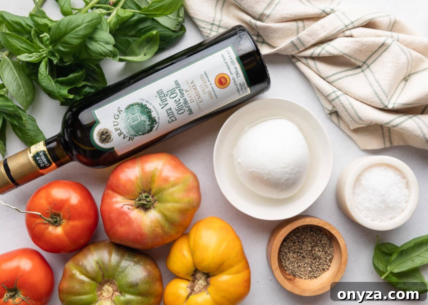 Fresh Caprese Salad 3 overhead photo of ingredients needed to make caprese salad: heirloom tomatoes, fresh basil, buffalo mozzarella in a white bowl, salt, pepper, and a bottle of olive oil
