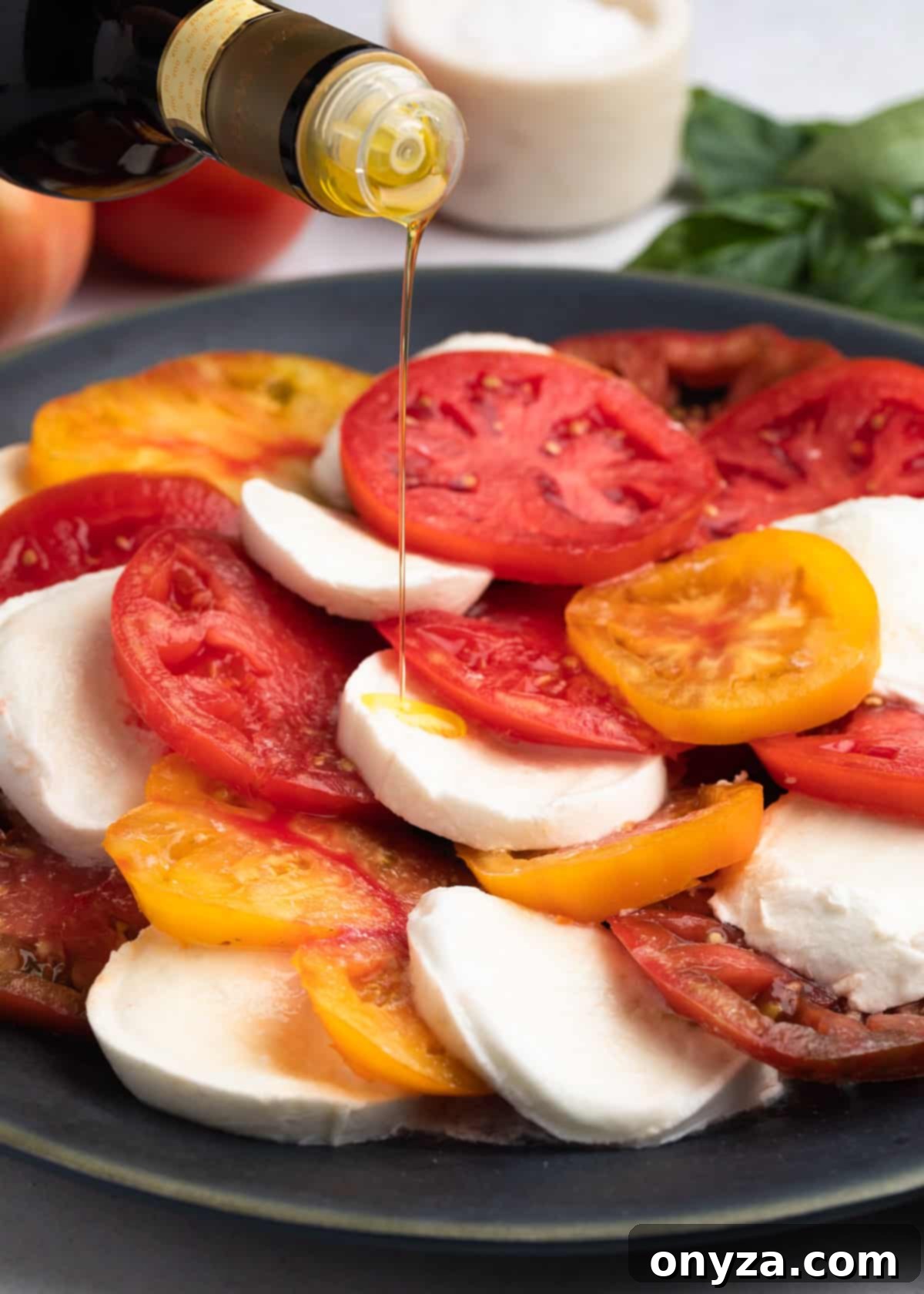 Fresh Caprese Salad 6 extra virgin olive oil being drizzled over a caprese salad on a gray platter