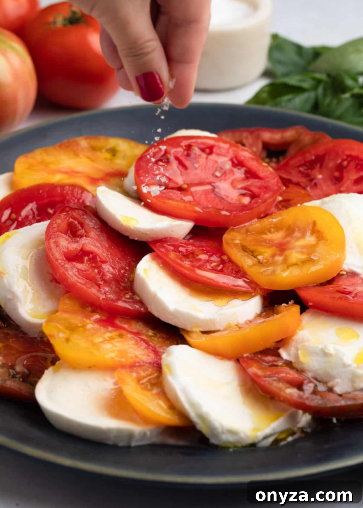 Fresh Caprese Salad 7 sea salt being sprinkled over a caprese salad on a round, dark gray platter