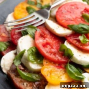 Fresh Caprese Salad 9 layered caprese salad with sliced mozzarella tomatoes and basil leaves on a dark gray plate with a fork