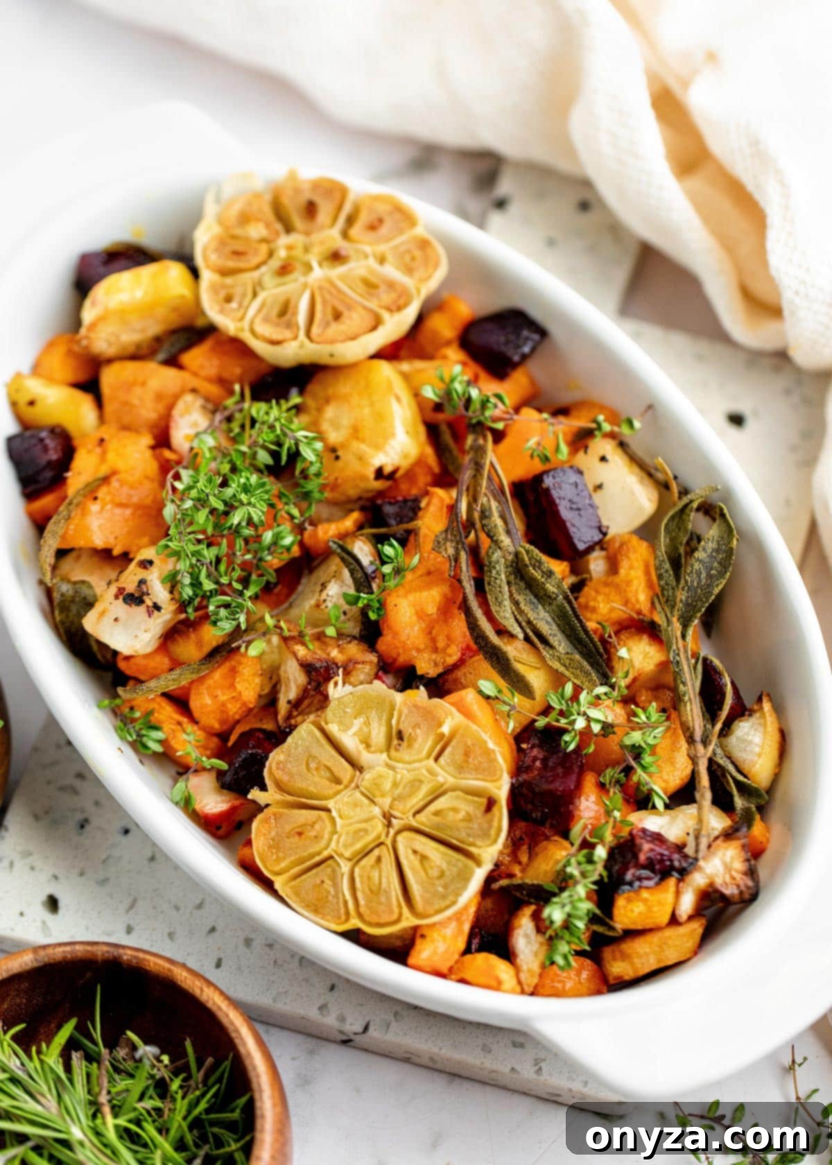 Assorted roasted root vegetables in a white gratin dish, garnished with fresh herbs, ready to be served.