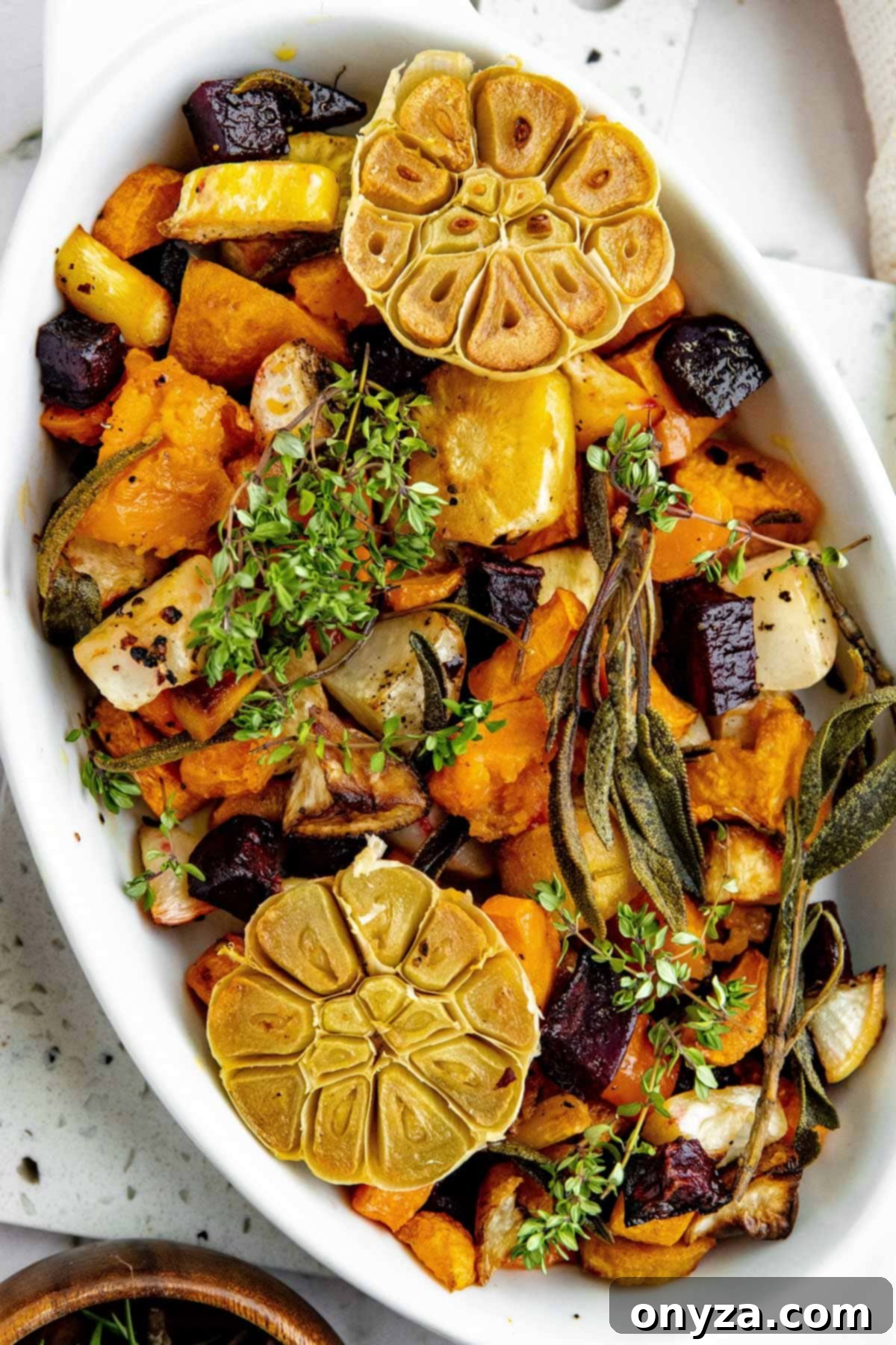 Overhead photo of roasted root vegetables in a pristine white gratin dish, elegantly garnished with fresh sprigs of herbs, ready to be enjoyed.