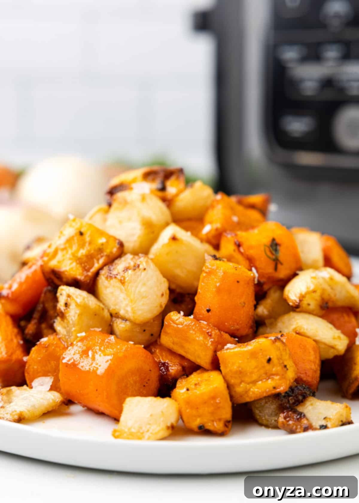 closeup of cooked root vegetables on a white platter with a black air fryer in the background