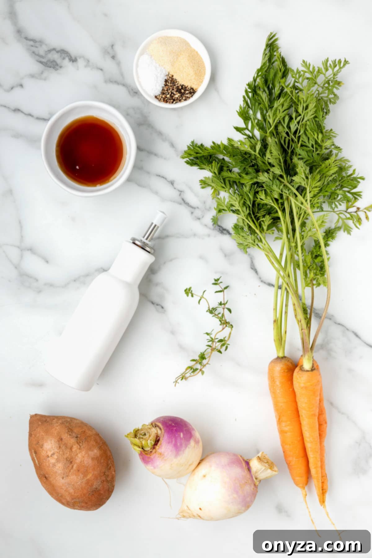 overhead photo of root vegetables, a bowl of maple syrup, dried spices, and a cruet of oil on a marble board.