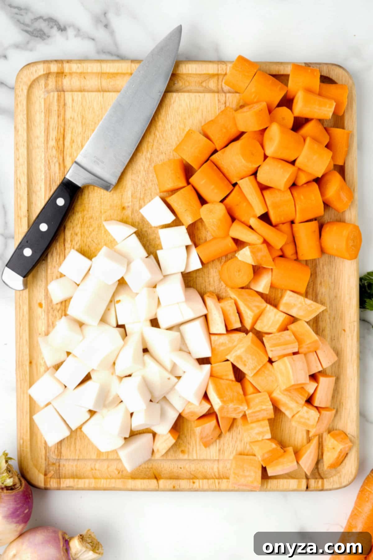 overhead photo of diced carrots, sweet potatoes, and turnips on a wooden cutting board with a chef's knife