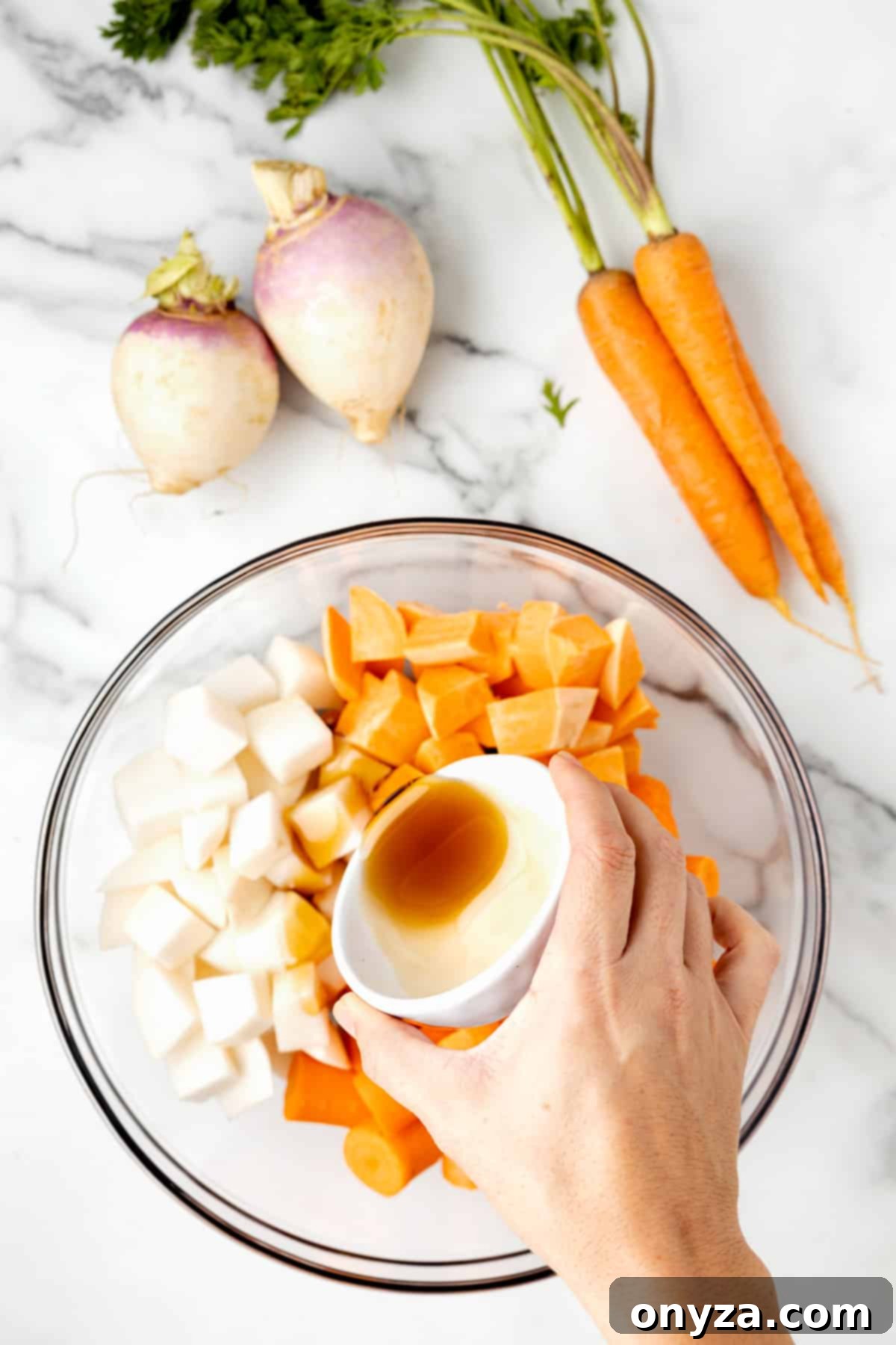overhead photo of cubed root vegetables in a glass bowl with maple syrup being poured over the top