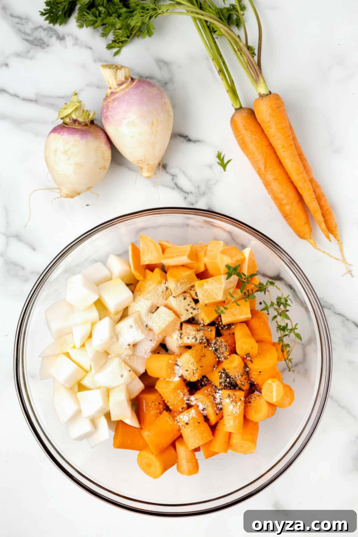 overhead photo of cubed root vegetables in a glass bowl on a white marble board, seasoned with dried spices and fresh thyme
