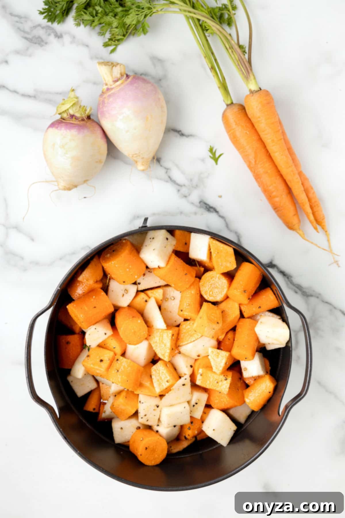 overhead photo of cubed raw root vegetables in a black air fryer basket on a white marble board