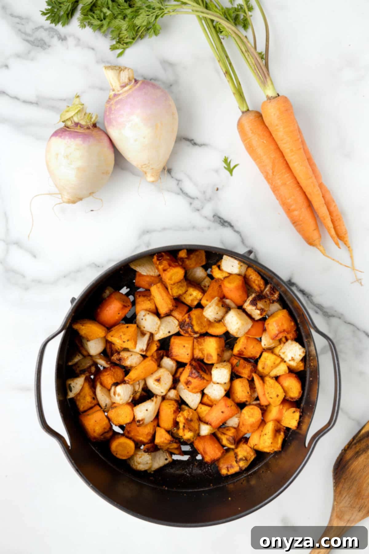 overhead photo of cooked cubed root vegetables in a black air fryer basket on a white marble board