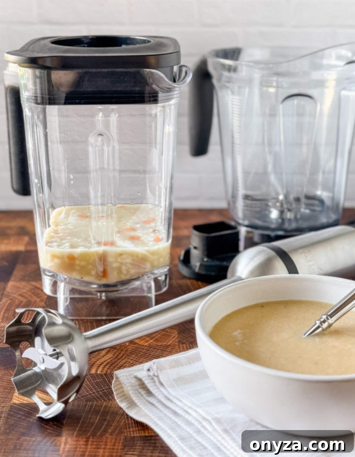 Safely Blend Hot Liquids Without the Mess 2 two blender jars, a stick blender, and a bowl of cream of chicken soup on a butcher block counter