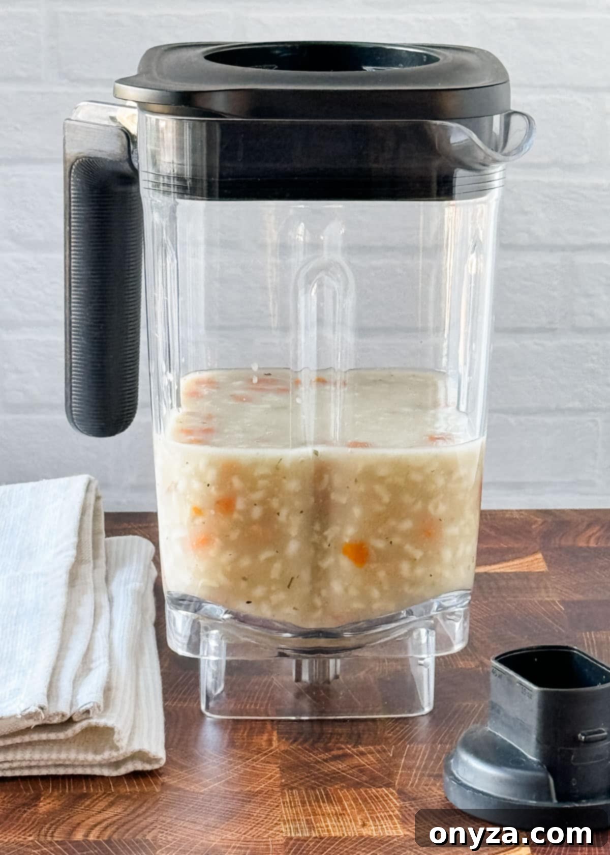Safely Blend Hot Liquids Without the Mess 3 blender jar filled halfway with chicken rice soup on a butcher block counter