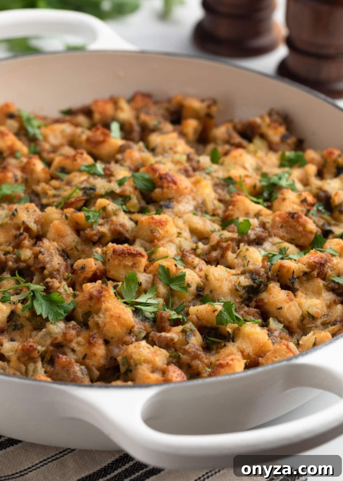 Baked Italian sausage stuffing in a white enameled cast iron gratin dish, golden brown and garnished with fresh parsley.