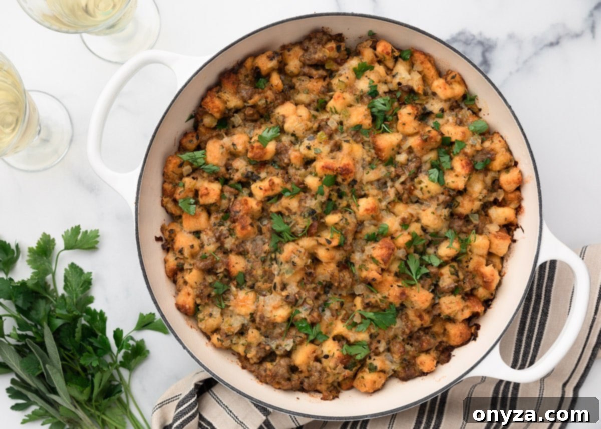 Overhead view of perfectly baked Italian sausage stuffing in a white braiser, golden and crisp on top, garnished with fresh parsley. Glasses of white wine and fresh herbs are arranged nearby for serving.