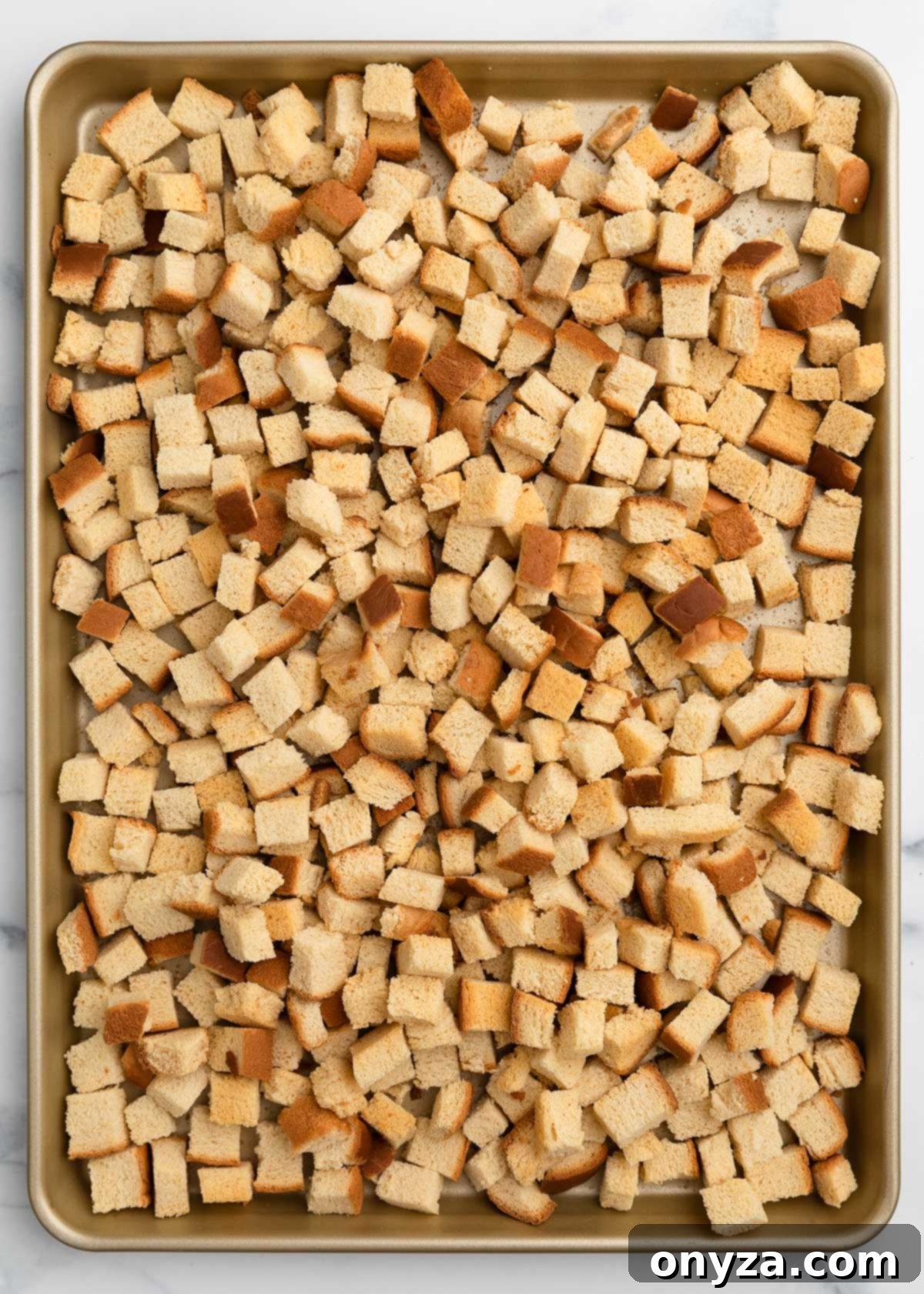 Perfectly baked and cooled country white bread croutons on a rimmed half sheet pan, lightly golden.