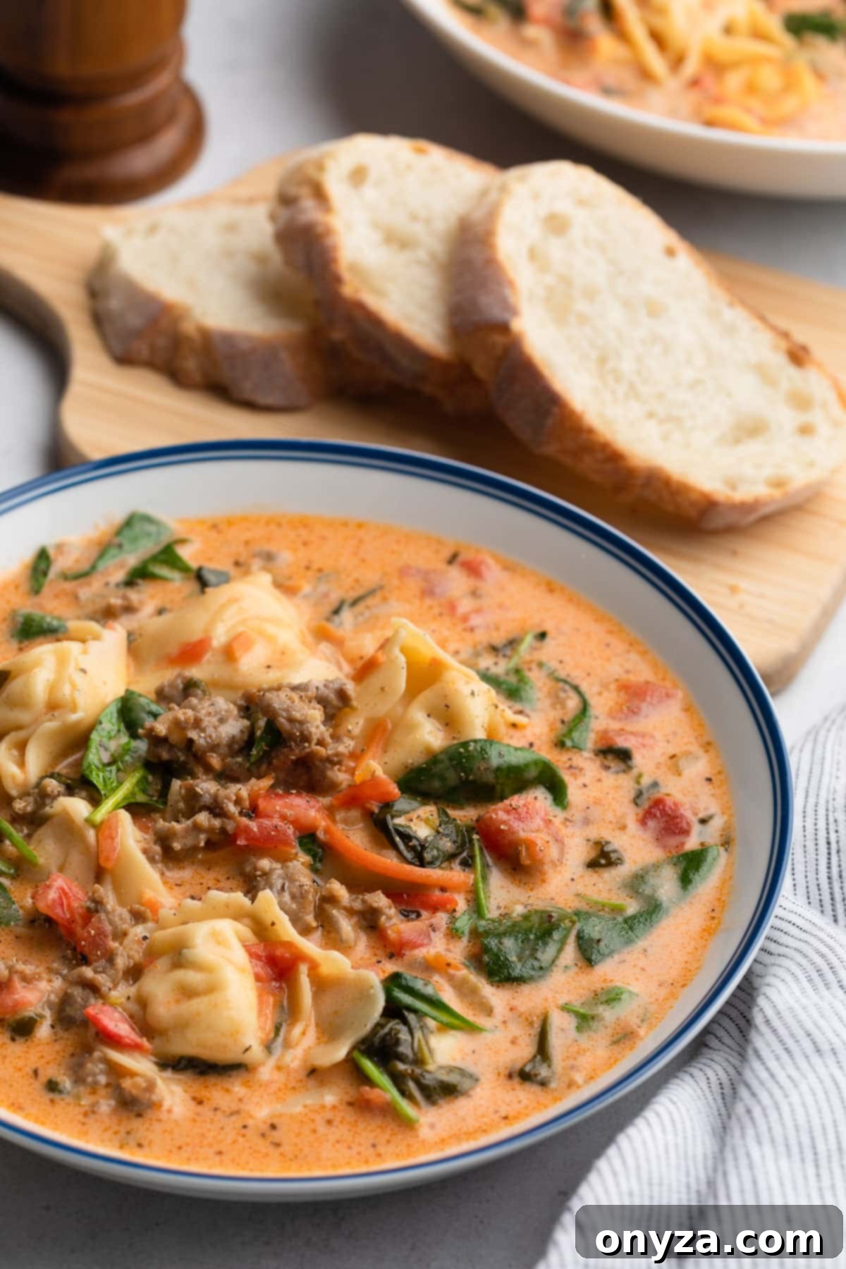 A vibrant bowl of Creamy Sausage Tortellini Soup, featuring rich tomato-Parmesan broth, succulent Italian sausage, and tender cheese tortellini, served with crusty Italian bread on a wooden board.