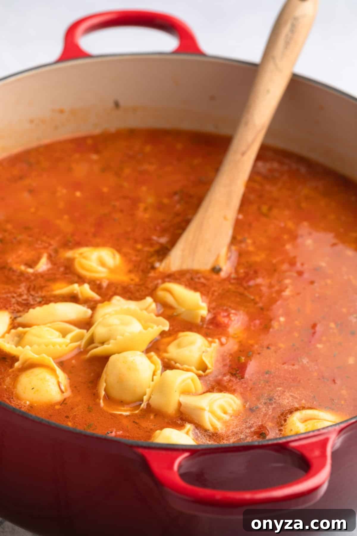 Fresh, uncooked refrigerated tortelloni being gently added to a simmering pot of Creamy Sausage Tortellini Soup, ready to cook to al dente perfection.