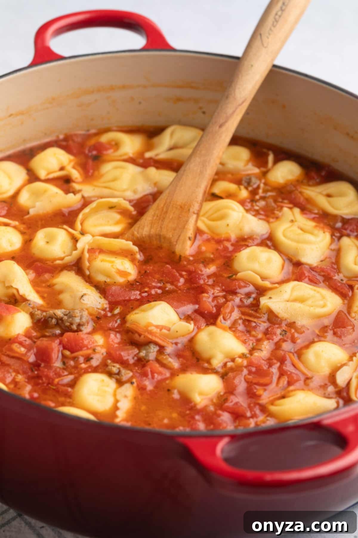 Perfectly cooked cheese tortelloni nestled in a rich tomato-based broth, served in a red enameled cast iron Dutch oven with a wooden spoon, ready for the finishing touches.