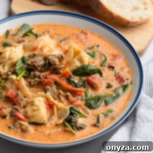 A comforting bowl of Creamy Tortellini Sausage Soup, presented in a blue-rimmed white ceramic bowl, perfectly garnished and ready to be enjoyed.