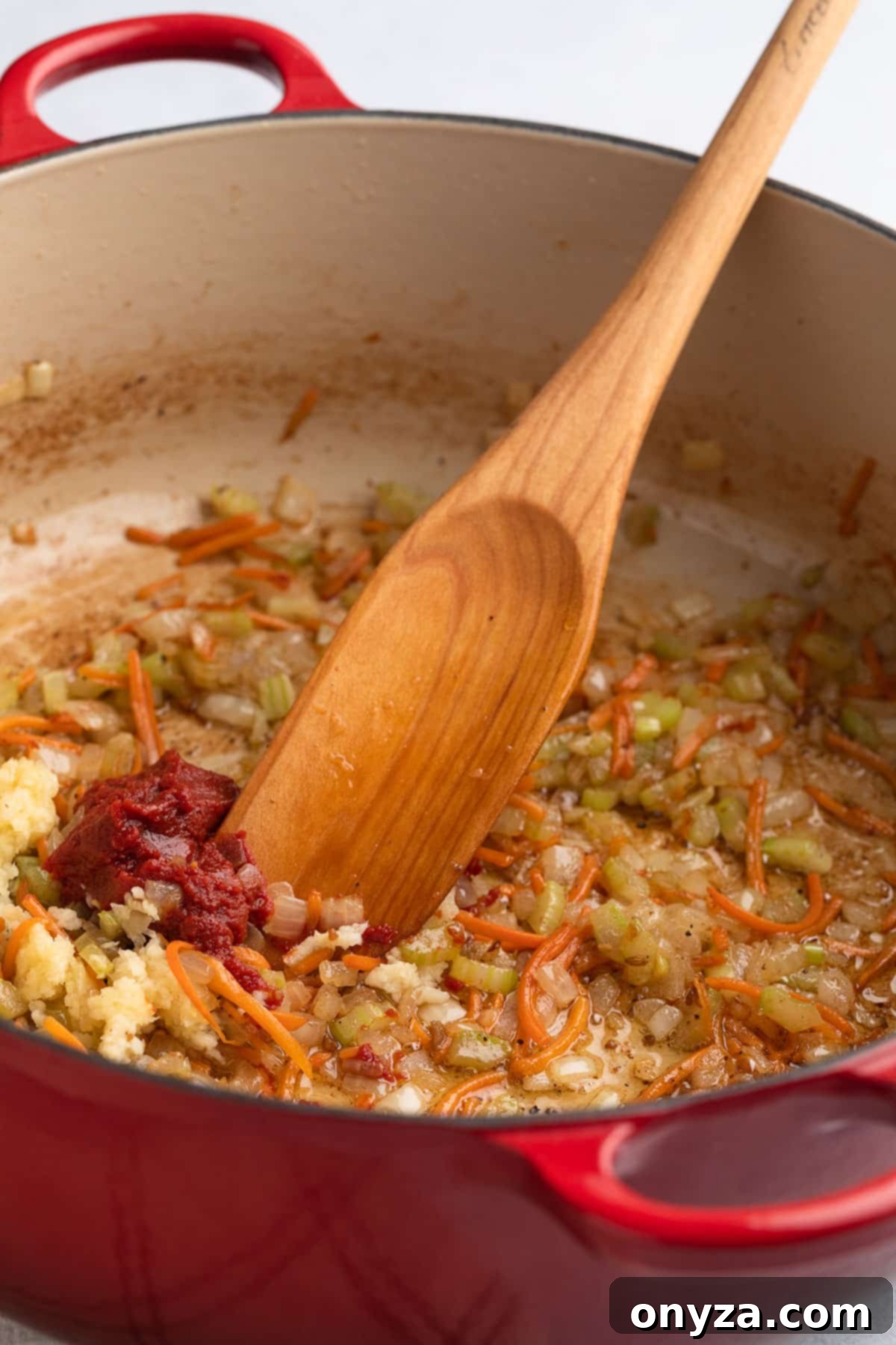 Sautéed onions, carrots, and celery in a Dutch oven with a dollop of double-concentrated tomato paste and fragrant minced garlic, ready to be stirred into the aromatic base.