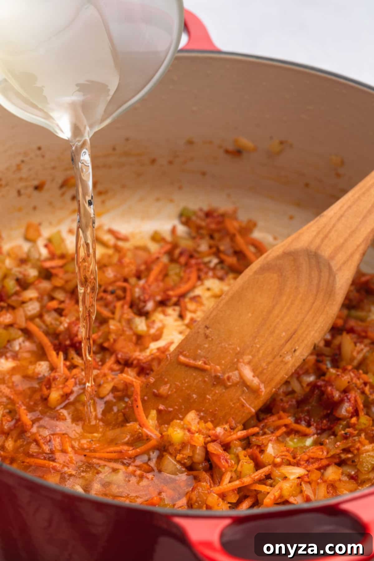 White wine being poured from a glass measuring cup into sautéed aromatics and cooked tomato paste in a red enameled Dutch oven, initiating the deglazing process.