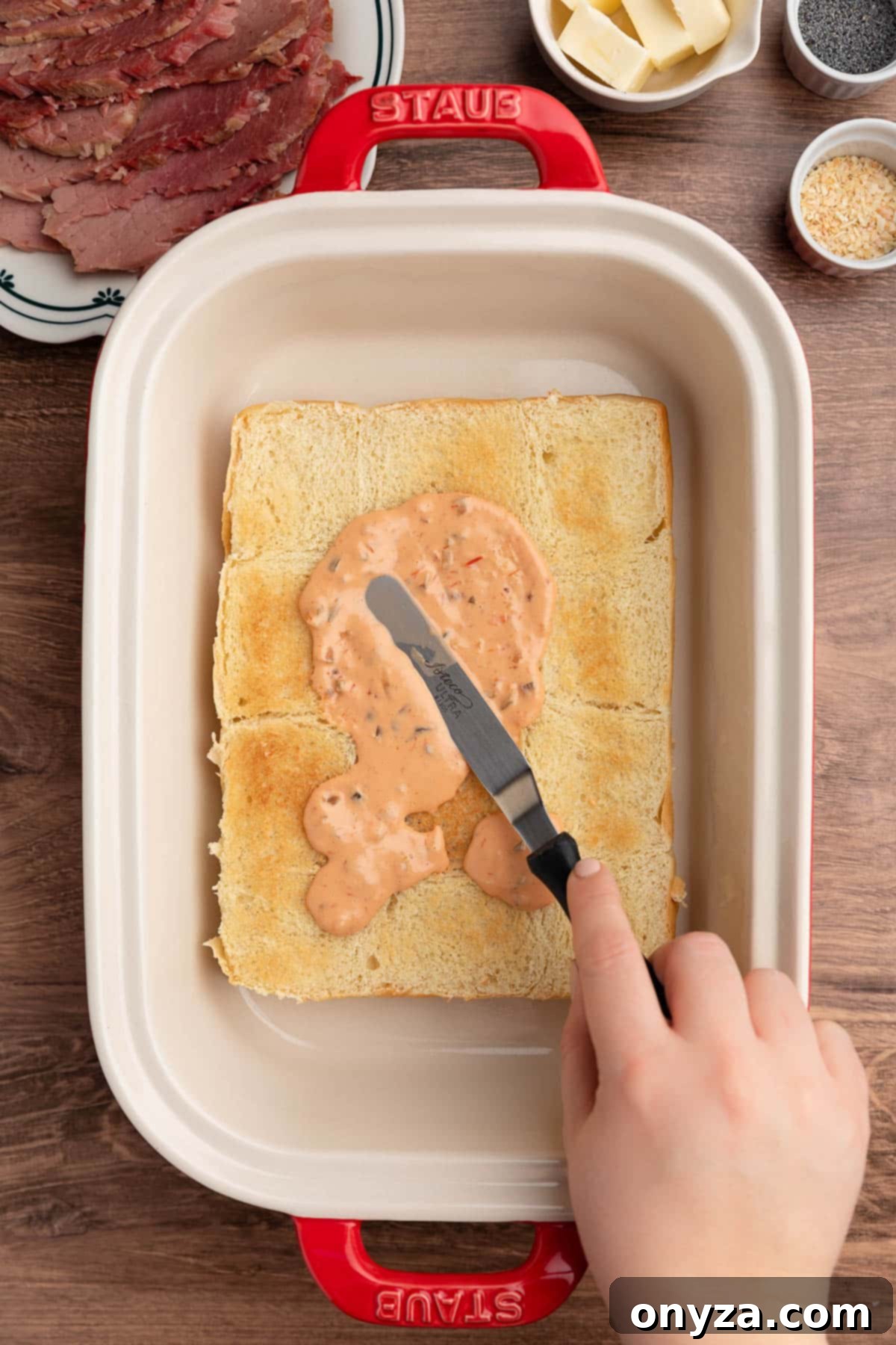 overhead photo of toasted slider bun bottoms in a ceramic baking dish being spread with Russian dressing