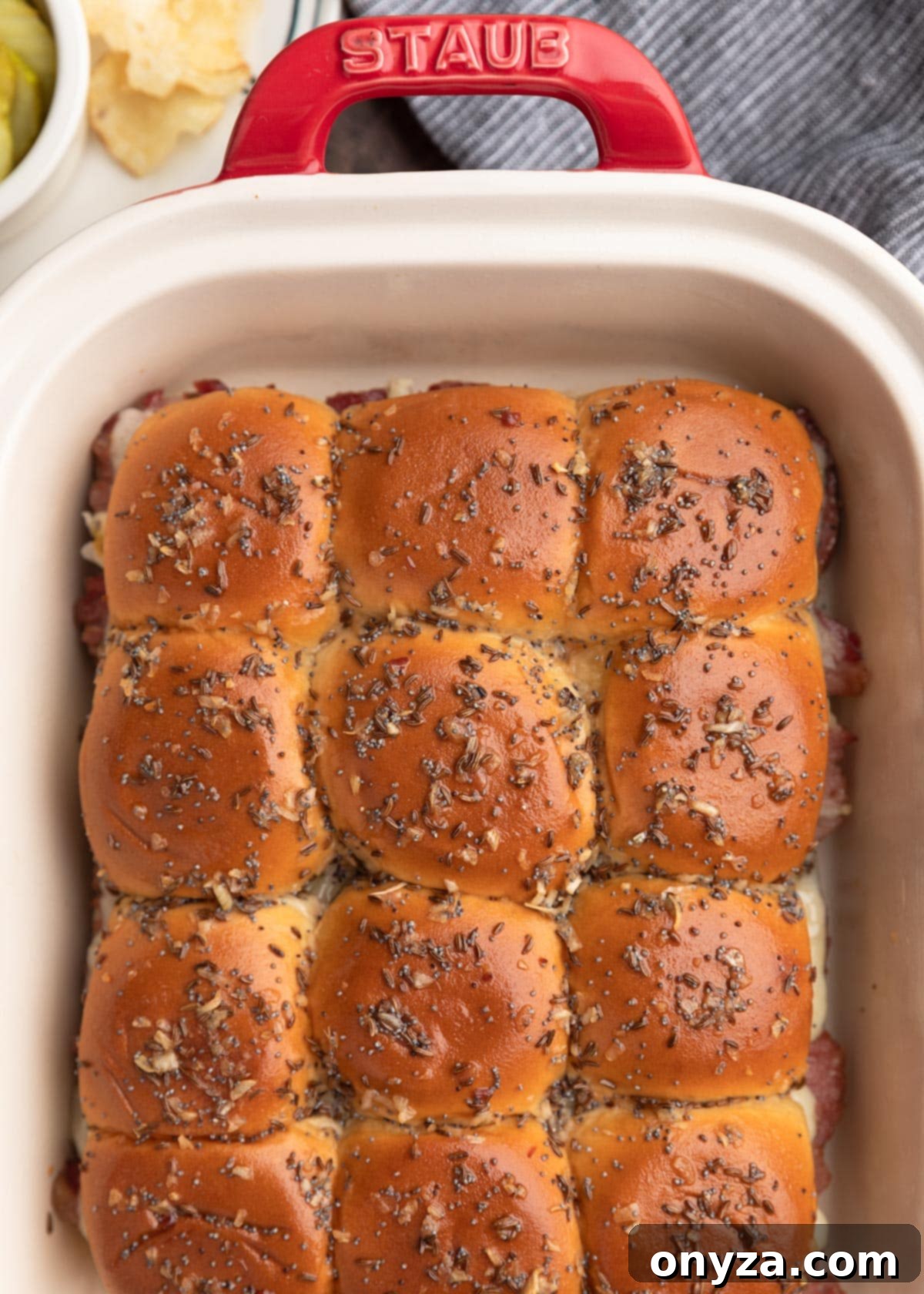 overhead photo of baked reuben sliders in a red and ivory Staub ceramic baking dish