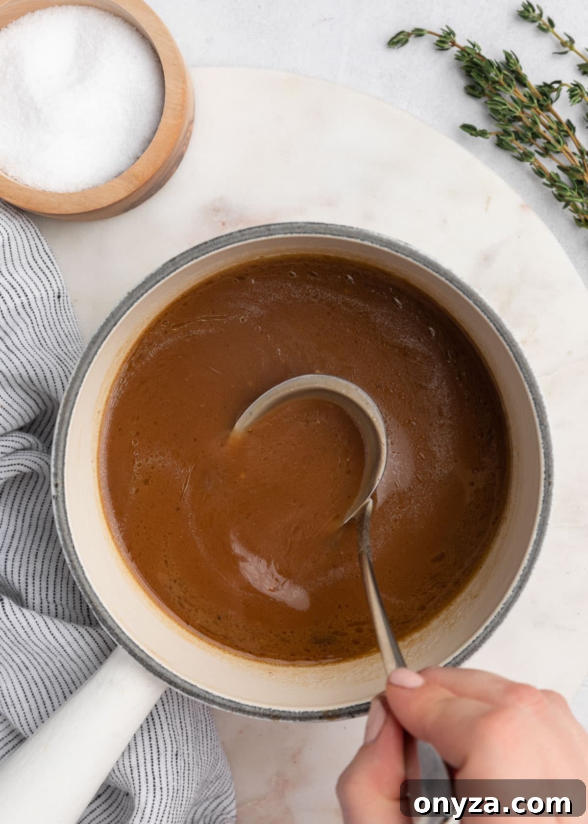 Savory French Dip Sliders 11 overhead photo of beef jus with a ladle in a white pot on a marble board