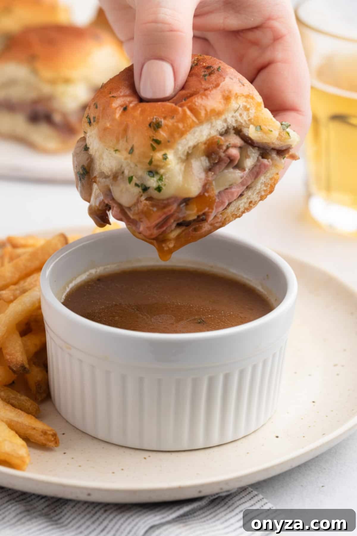 Savory French Dip Sliders 13 roast beef slider being dipped into a white ramekin of jus
