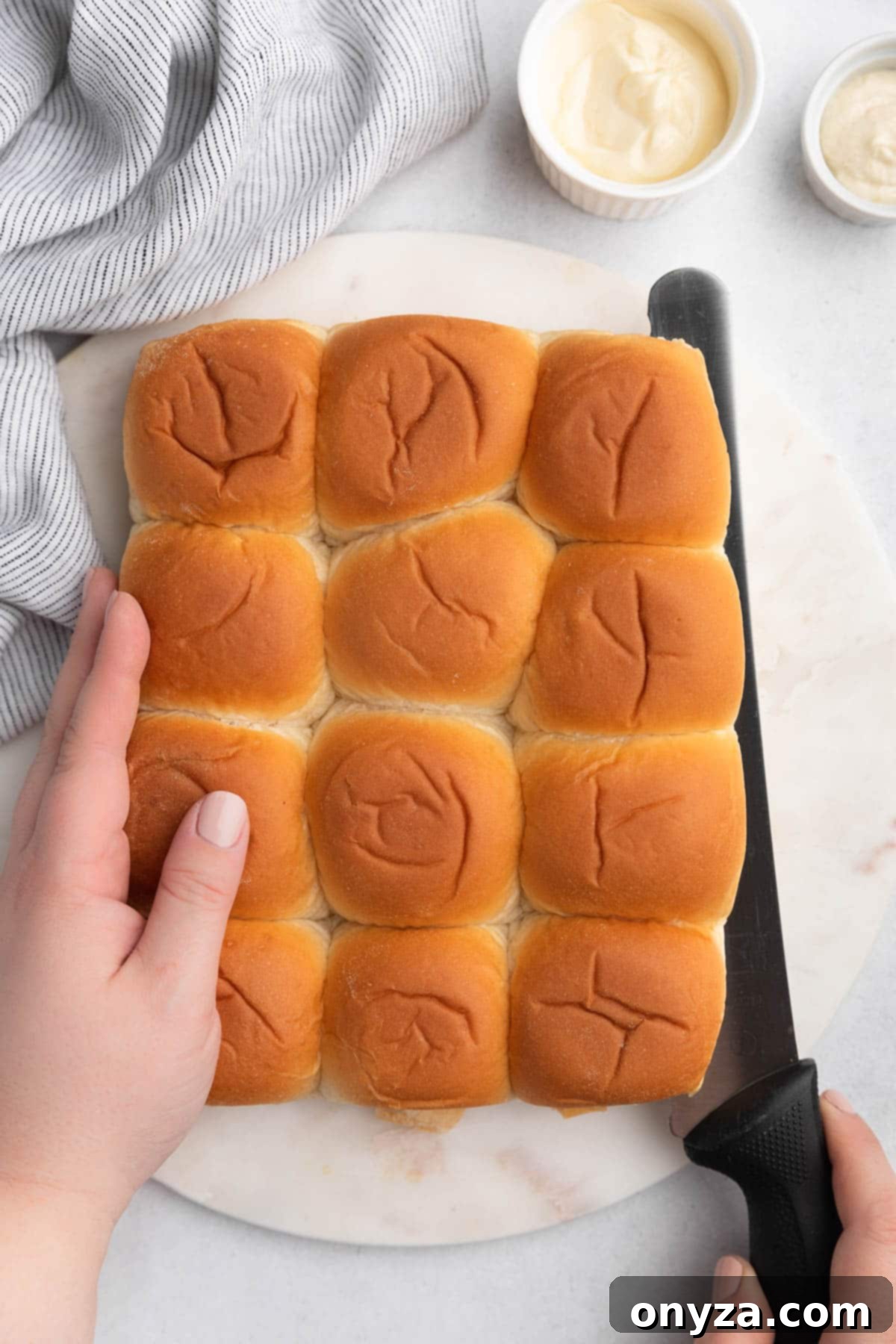 Savory French Dip Sliders 5 slider rolls being sliced on a white marble board