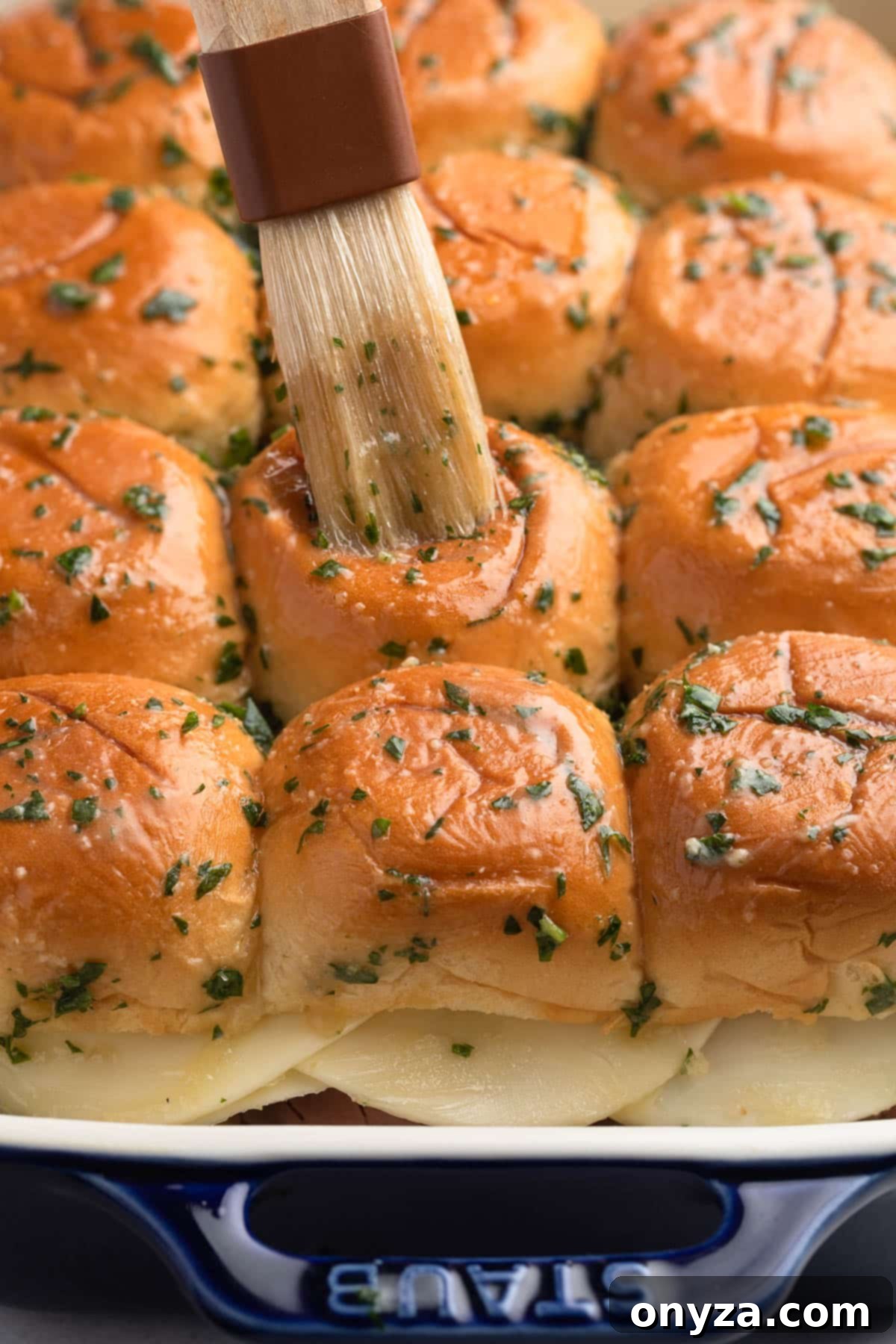 Savory French Dip Sliders 9 spreading butter sauce over French dip sliders in a baking dish with a pastry brush