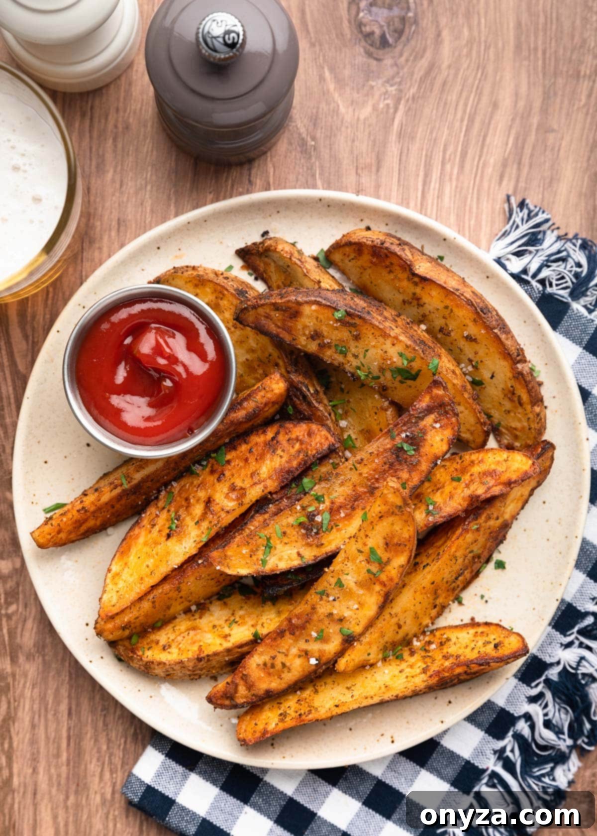 overhead of air fryer potato wedges on an ivory speckled plate with a condiment cup of ketchup. The plate is on a blue and white checked napkin.