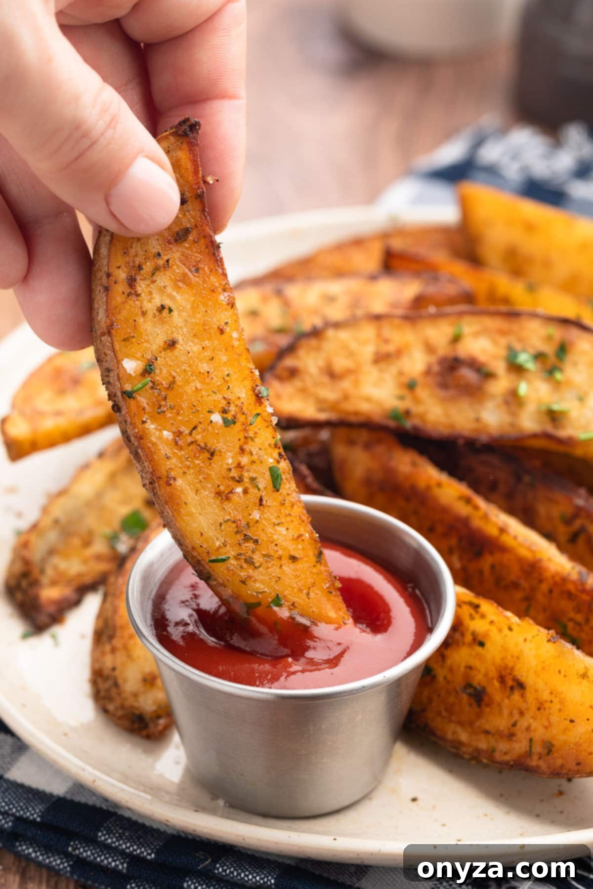 dipping an air fried potato wedge into a condiment cup of ketchup on a plate of the wedges