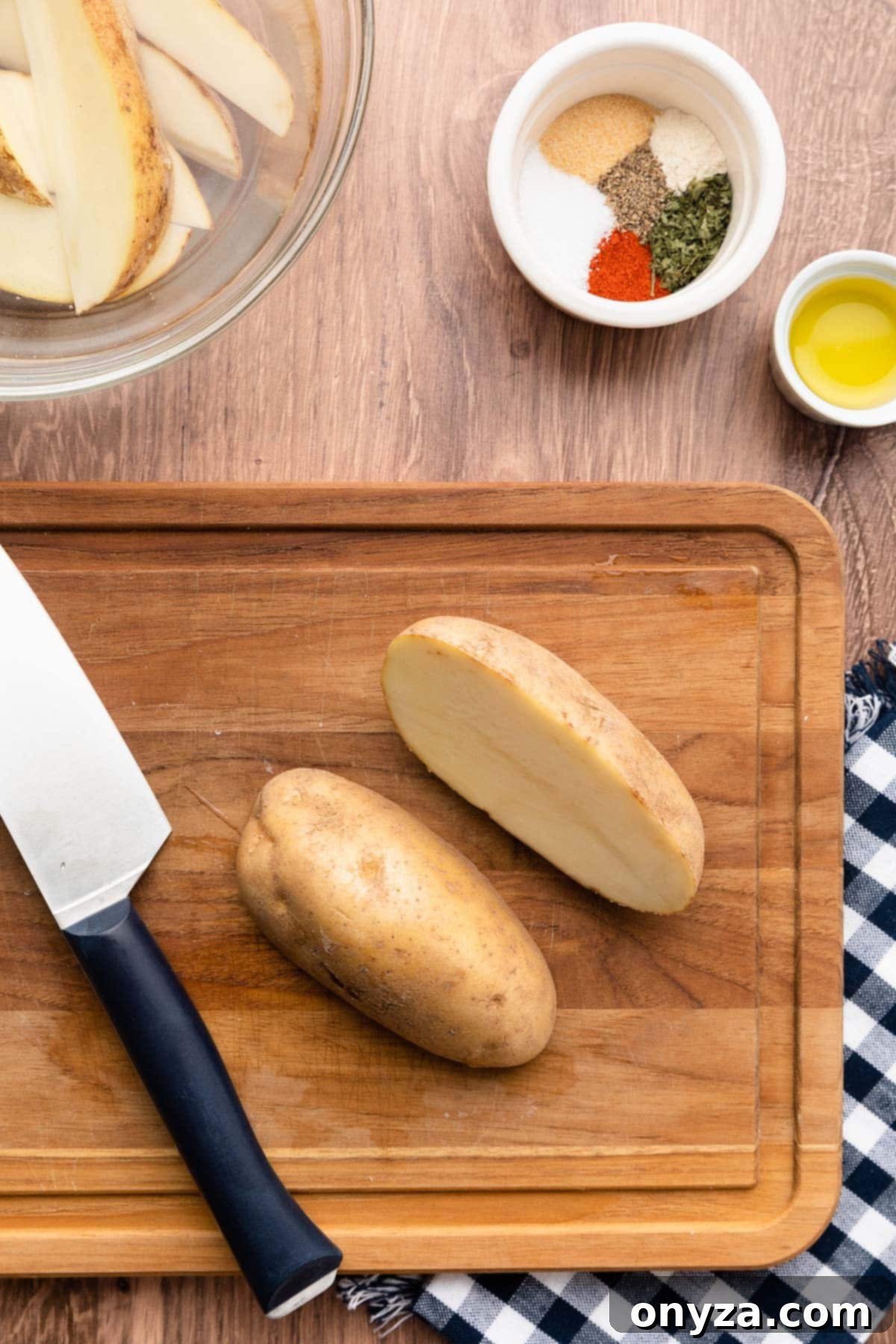 halved russet potato on a wood cutting board next to a chef's knife