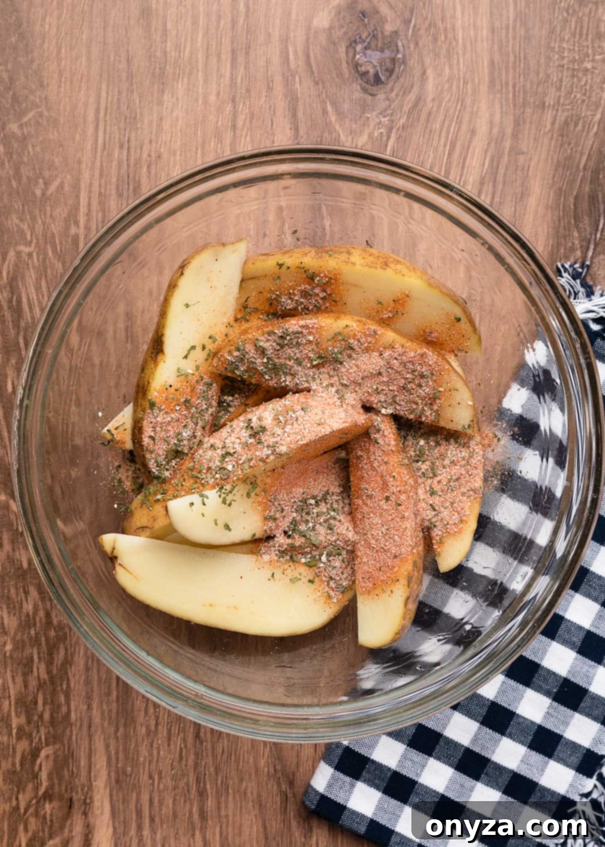 wedged russet potatoes in a glass bowl with olive oil and sprinkled with ground spices